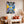 Cuadro de collage urbano amarillo y lila en MDF en sala con sofá crema, cojines terracota y pampas